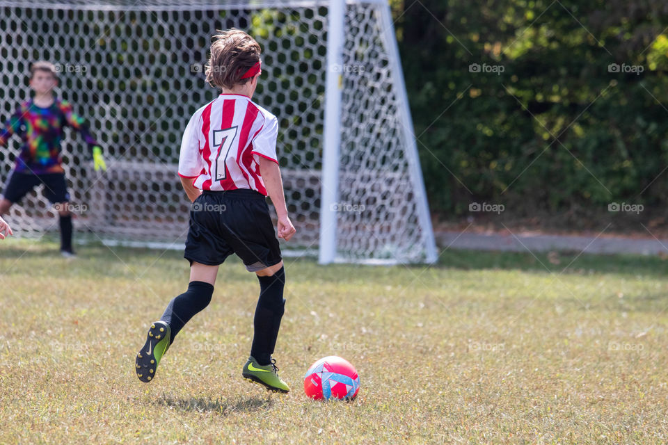 A boy kicking a soccer ball at the goal