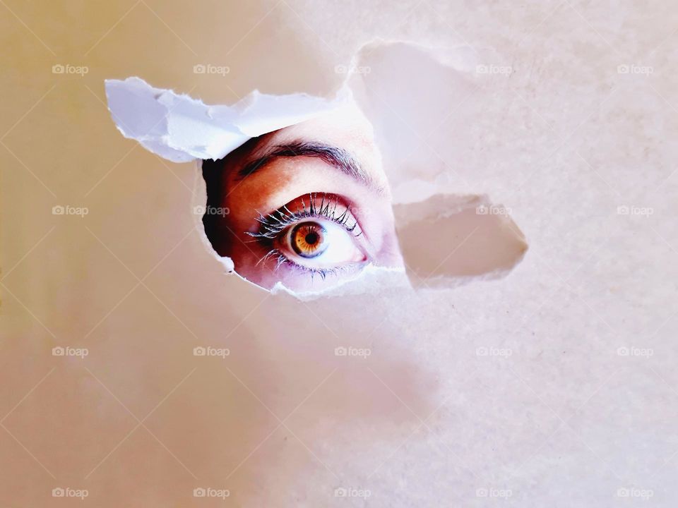 behind a torn white sheet there is a hazelnut woman's eye illuminated by the sunlight