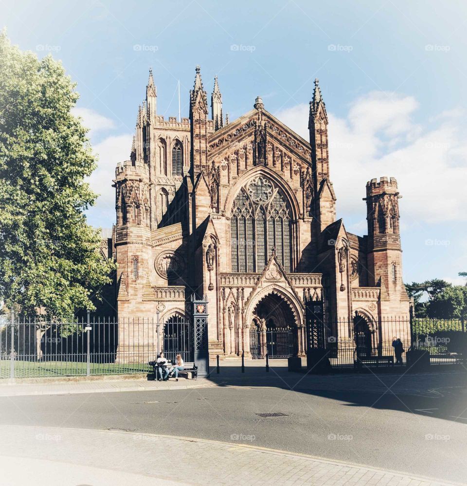 The beautiful Hereford Cathedral, taken in the height of summer. Tourists can be seen resting on the bench and the greenery in the background really enhances the scene.