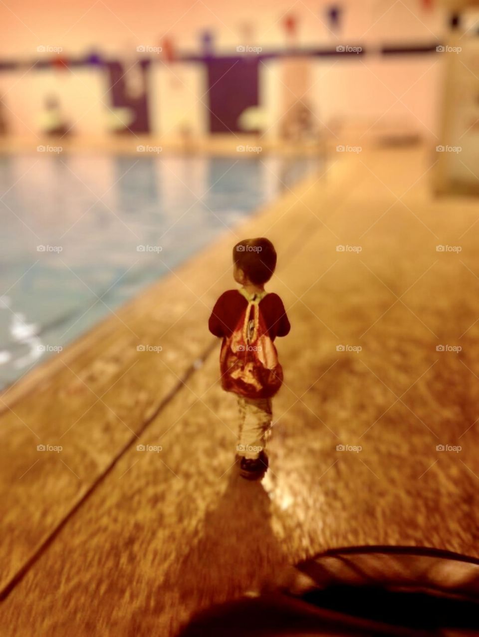 A young child carries his backpack to the swimming pool. 