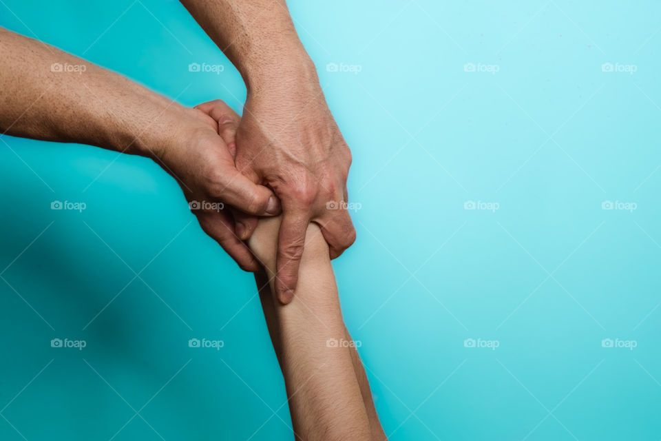 Intertwined hands of a young man and woman. On blue background.
