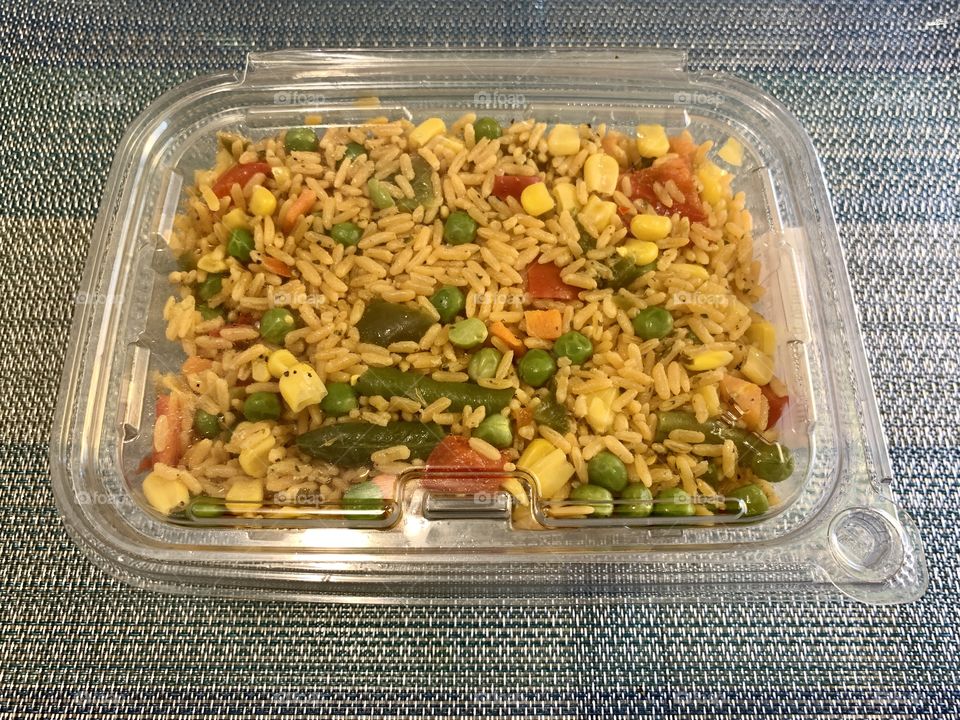 Rice and mix vegetables in a transparent container with sky blue background. Lunch and dinner. To go. Sealed.