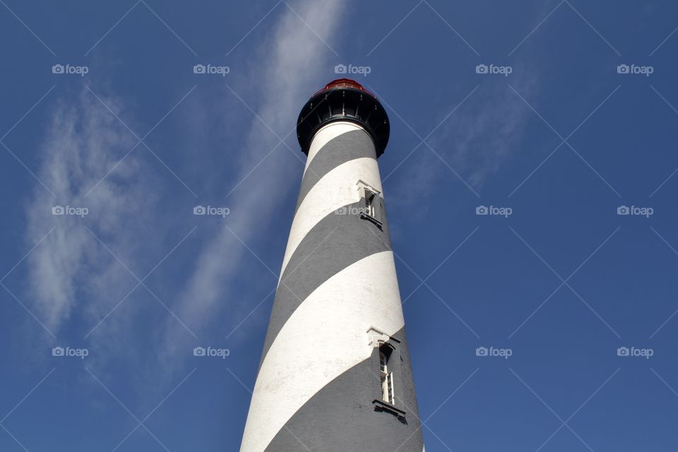 Looking up at a tall lighthouse with black and white stripes against a blue sky with white clouds 