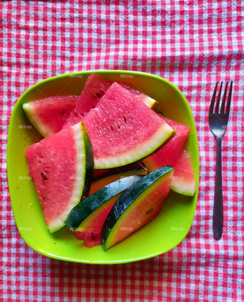 freshly cut watermelon on a green bowl in the kitchen with a fork. let's have some because it's summer time !🙂