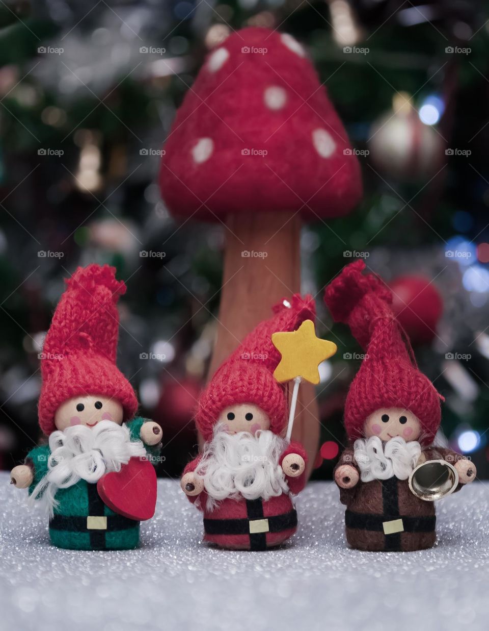 3 small wooden Christmas folk with knitted hats and white beards stand in front of a red & white toadstool 