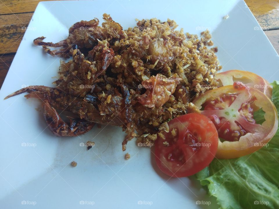 Fried soft shell crab with garlic, one of the most delicious and popular Thai food served in a white dish decorated with tomatoes and salad leaves.