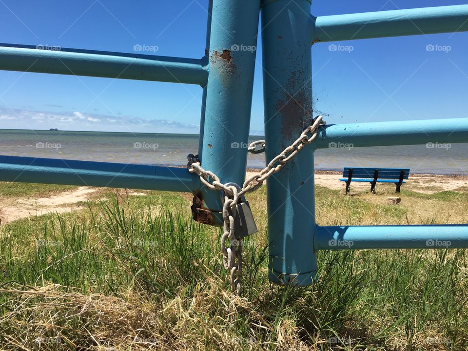 View of south Australian beach through weathered turquoise blue coloured metal fence licked with padlock 