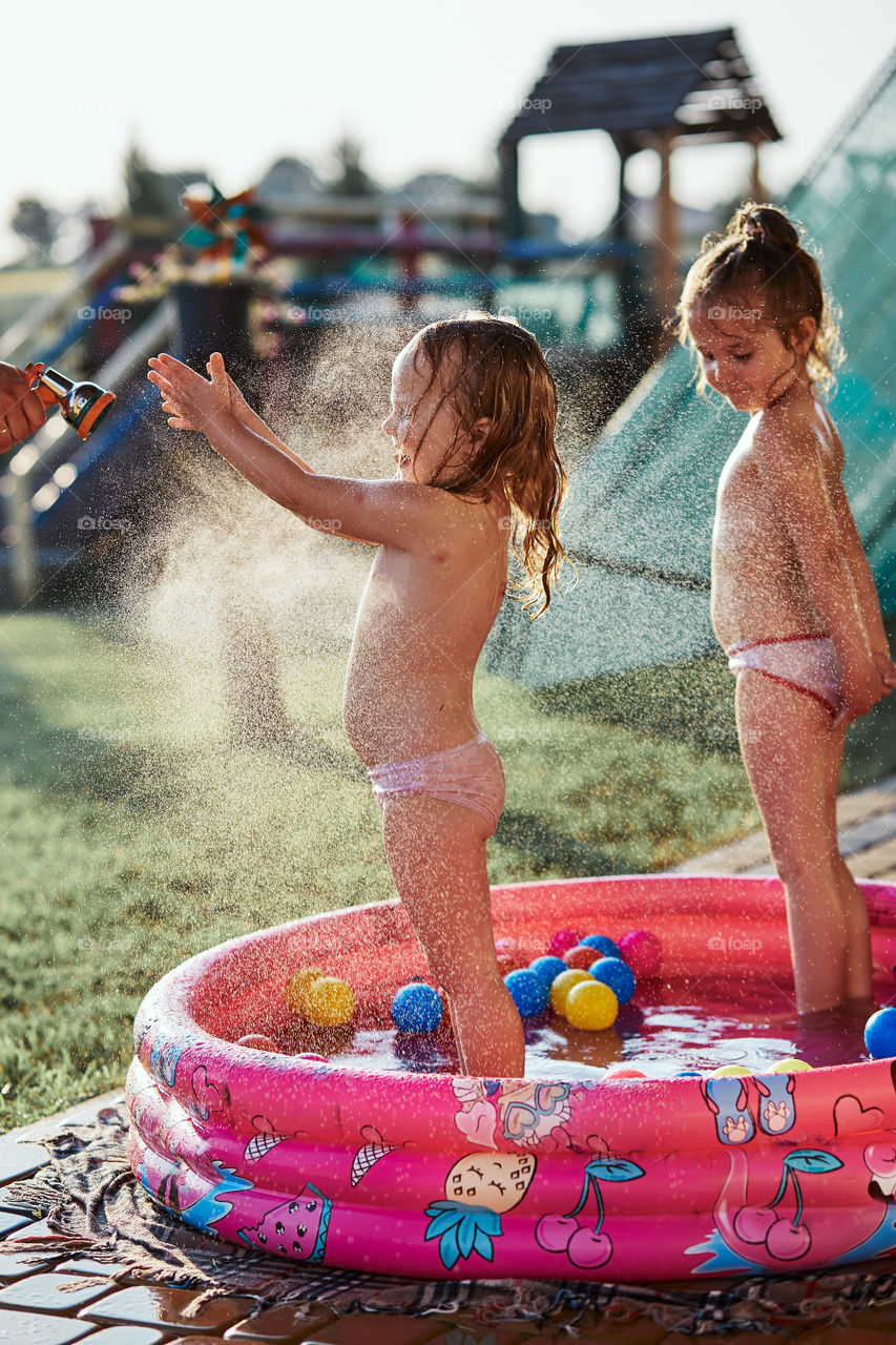 Little cute adorable girls enjoying a cool water sprayed by their father during hot summer day in backyard. Candid people, real moments, authentic situations