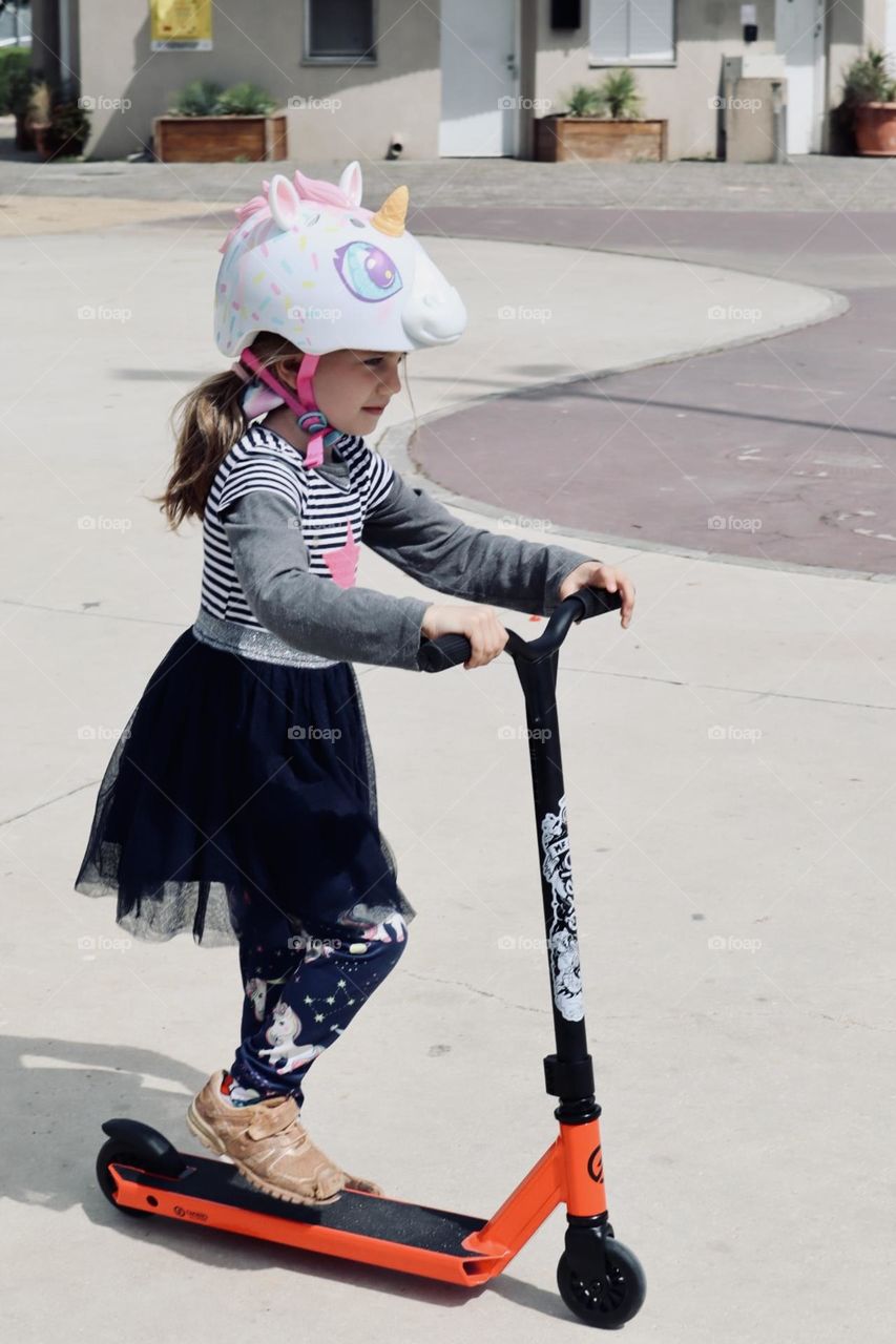 Girl with unicorn helmet riding her scooter 