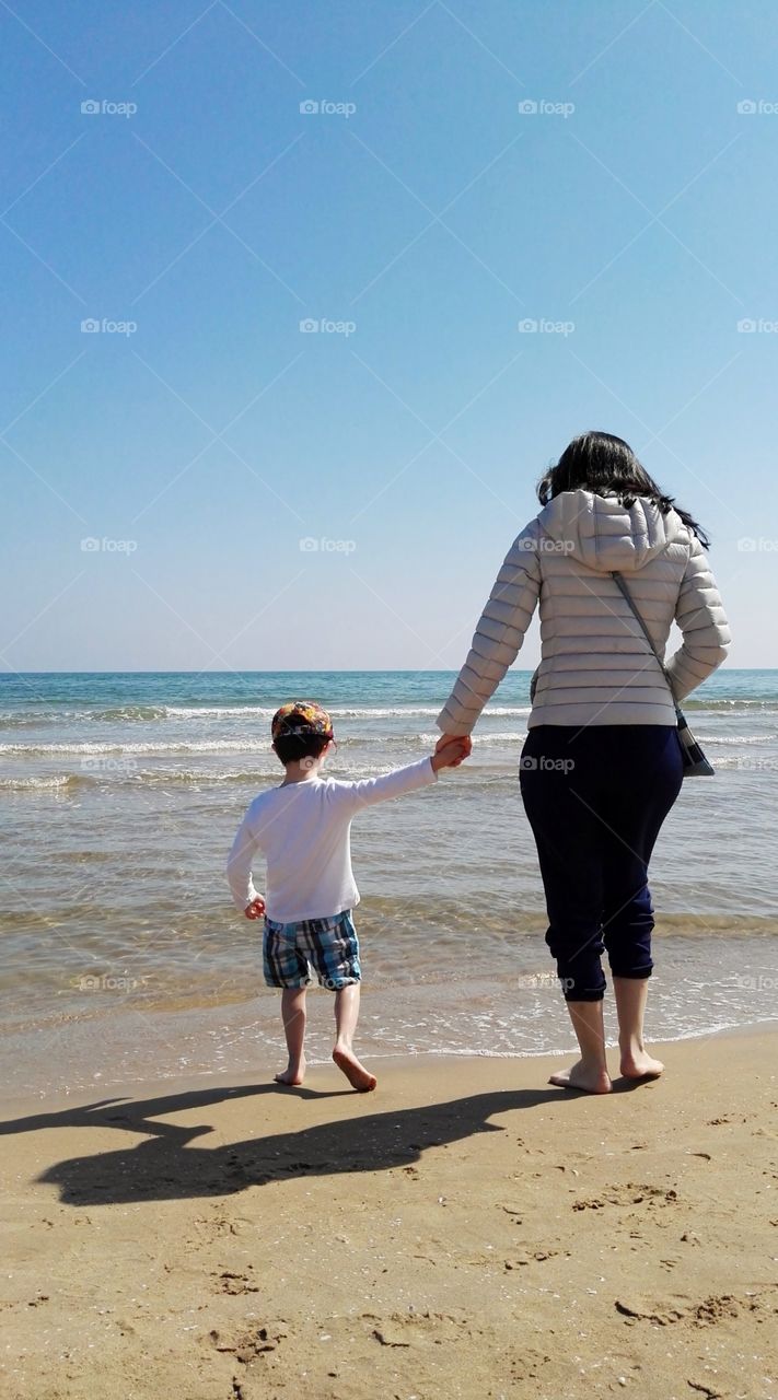 the mother and the son walking at the seashore looking at the waves