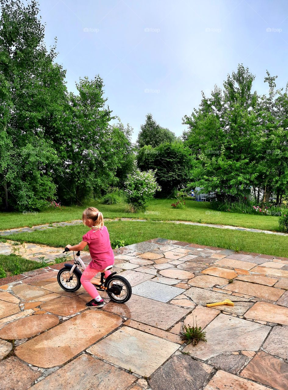 litlle girl on a bike  on stone terrace  in summer