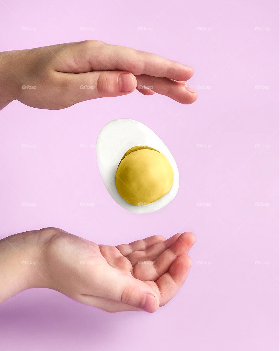 A half of egg flying between child’s hands, pink background 