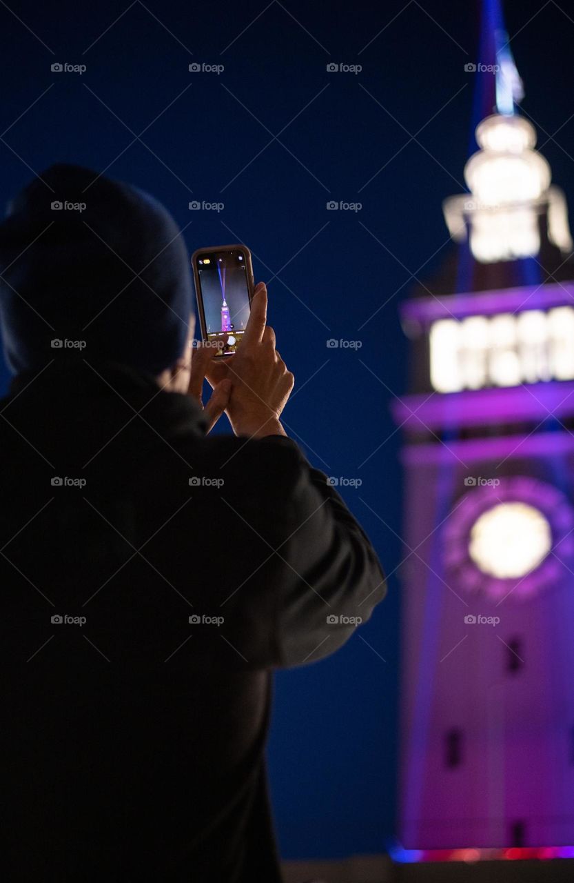 Man taking a photo of a tower at night 