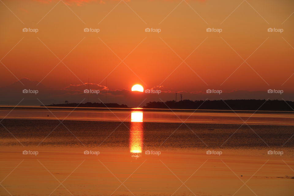 Sun rising above the ocean and the haze in the sky , bright light reflecting into the water as a column, promising a beautiful summer day