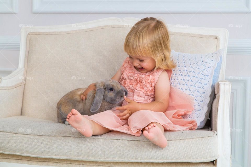 Cute baby girl playing with rabbit at home