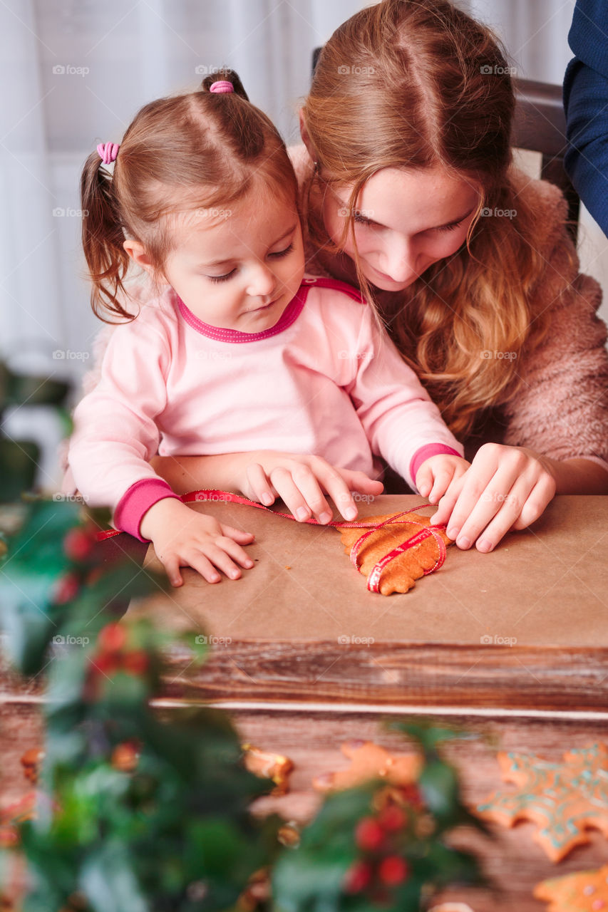 Girls tying baked Christmas gingerbread cookies with ribbon