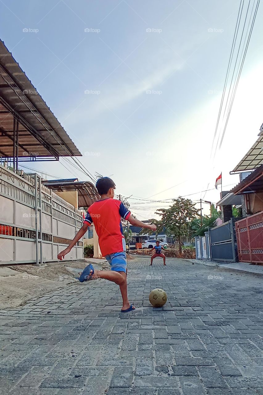 Bandar Lampung, Lampung, Indonesia - December 15, 2023: a child playing ball on the rocky road in front of the house