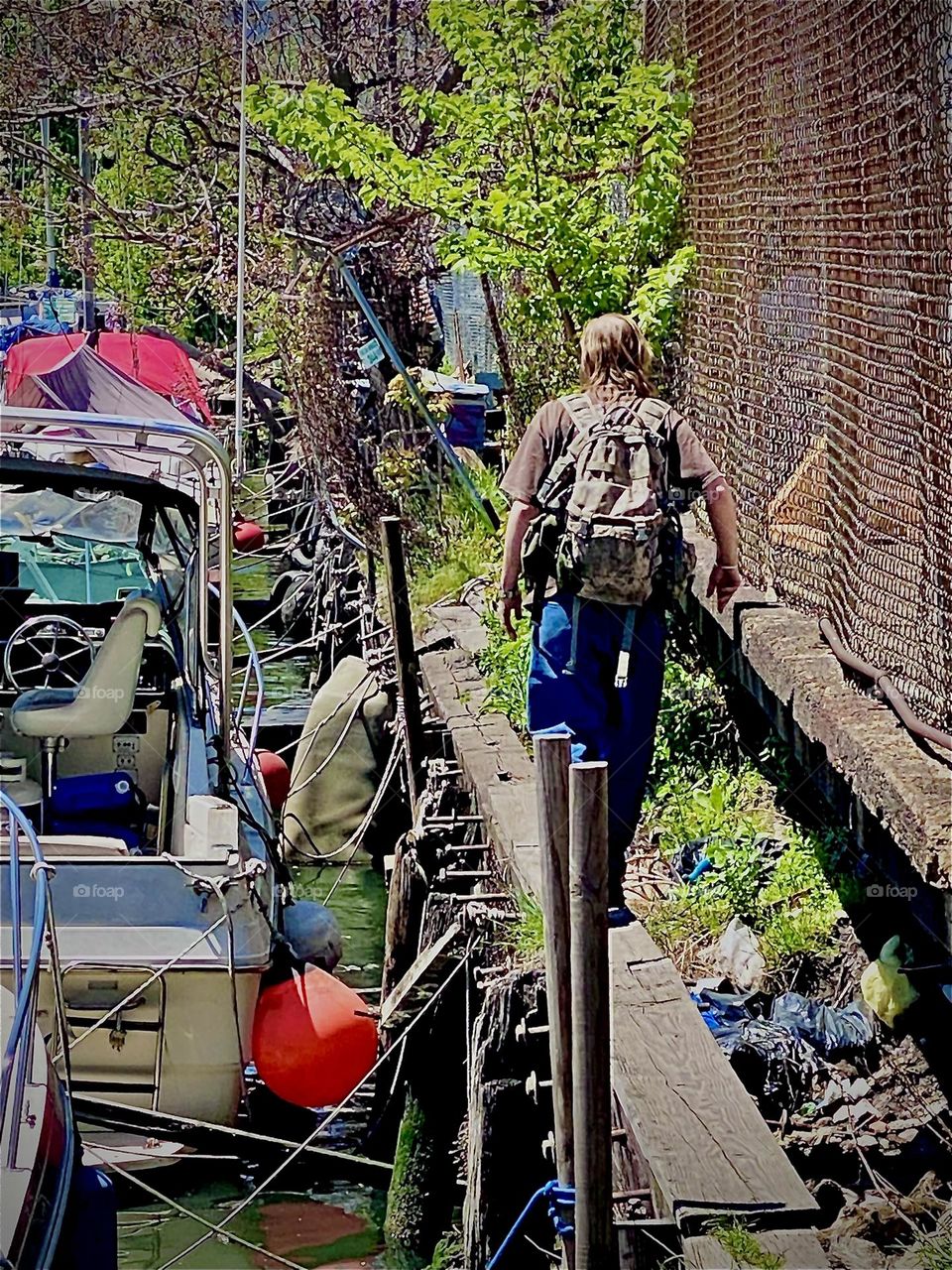 Timothy walks towards the „Salvation“, our boat that is also literally our salvation. The wooden planks lead along the wall to the various boats & ladders help to get down to the water at varying levels due to the tides. 2022. Hypnotic Productions