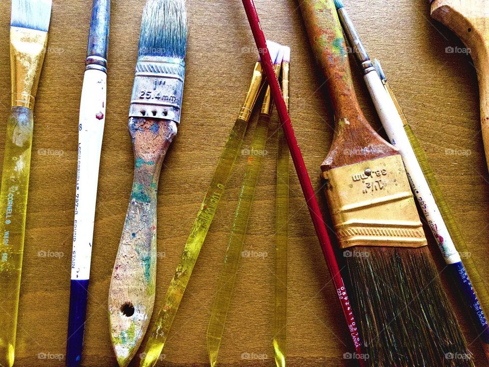 Overhead closeup of art workspace. Well used paintbrushes of various sizes form a still life of their own.