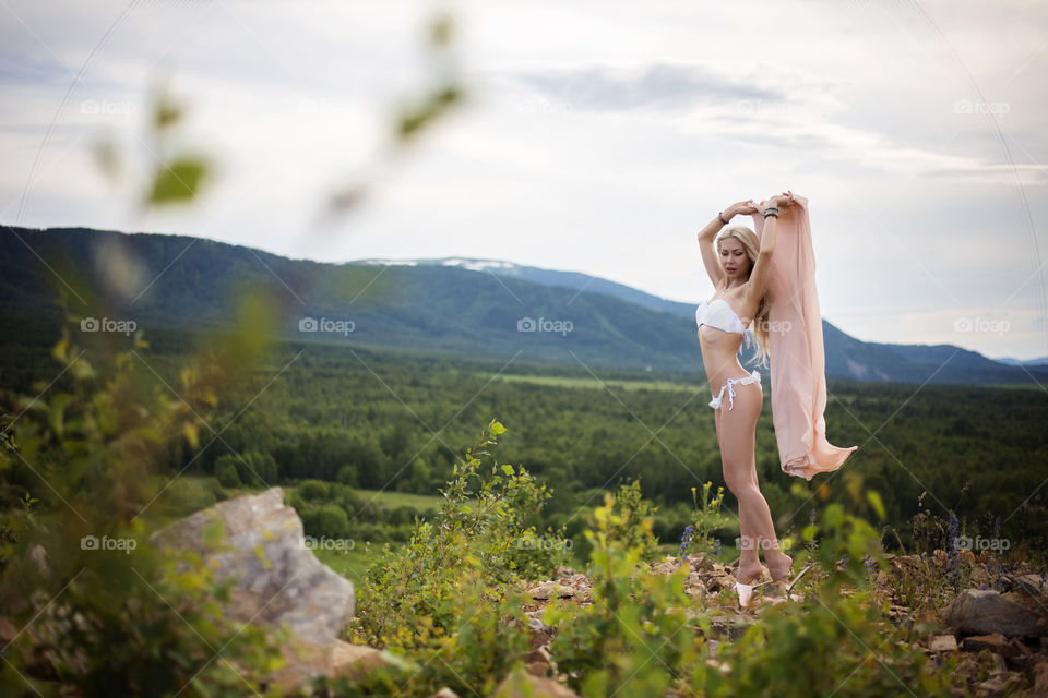 Woman in bikini blowing scarf against mountain