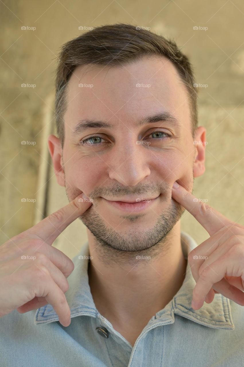 Portrait of a guy with dark hair who is smiling with hands near face