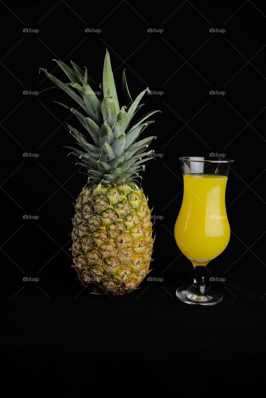 Pineapple with glass cup with juice on black background. Tropical fruit