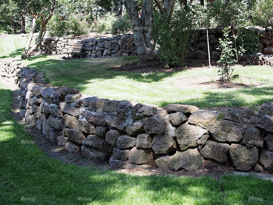 Multiple tiers with rock walls of different growth from grass to flowers and trees as well as a park bench  in Pioneer Park in Bend in Central Oregon on a beautiful sunny summer day. 