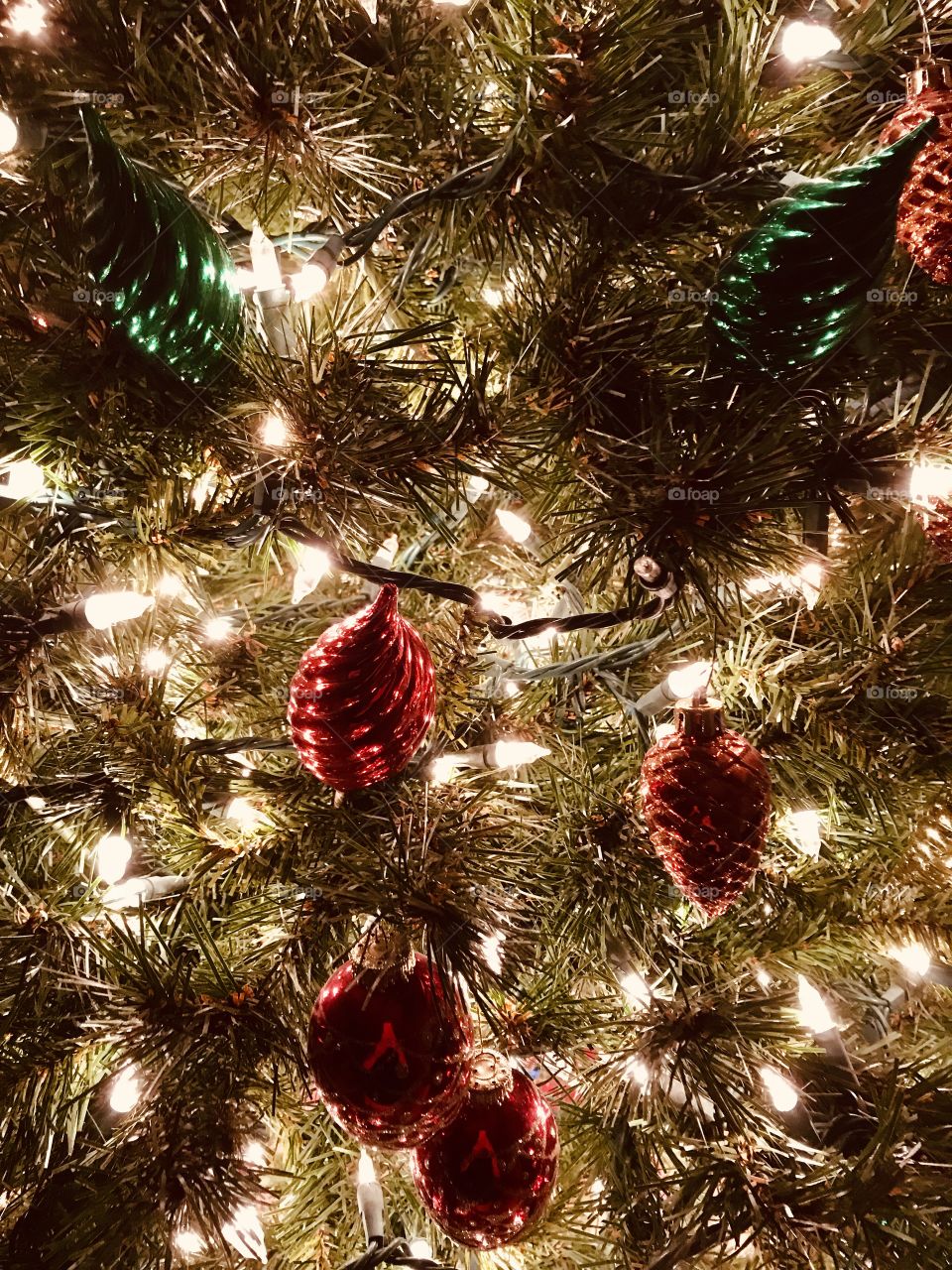 Close up of Christmas tree with white lights and red, gold and green shiny ornaments 