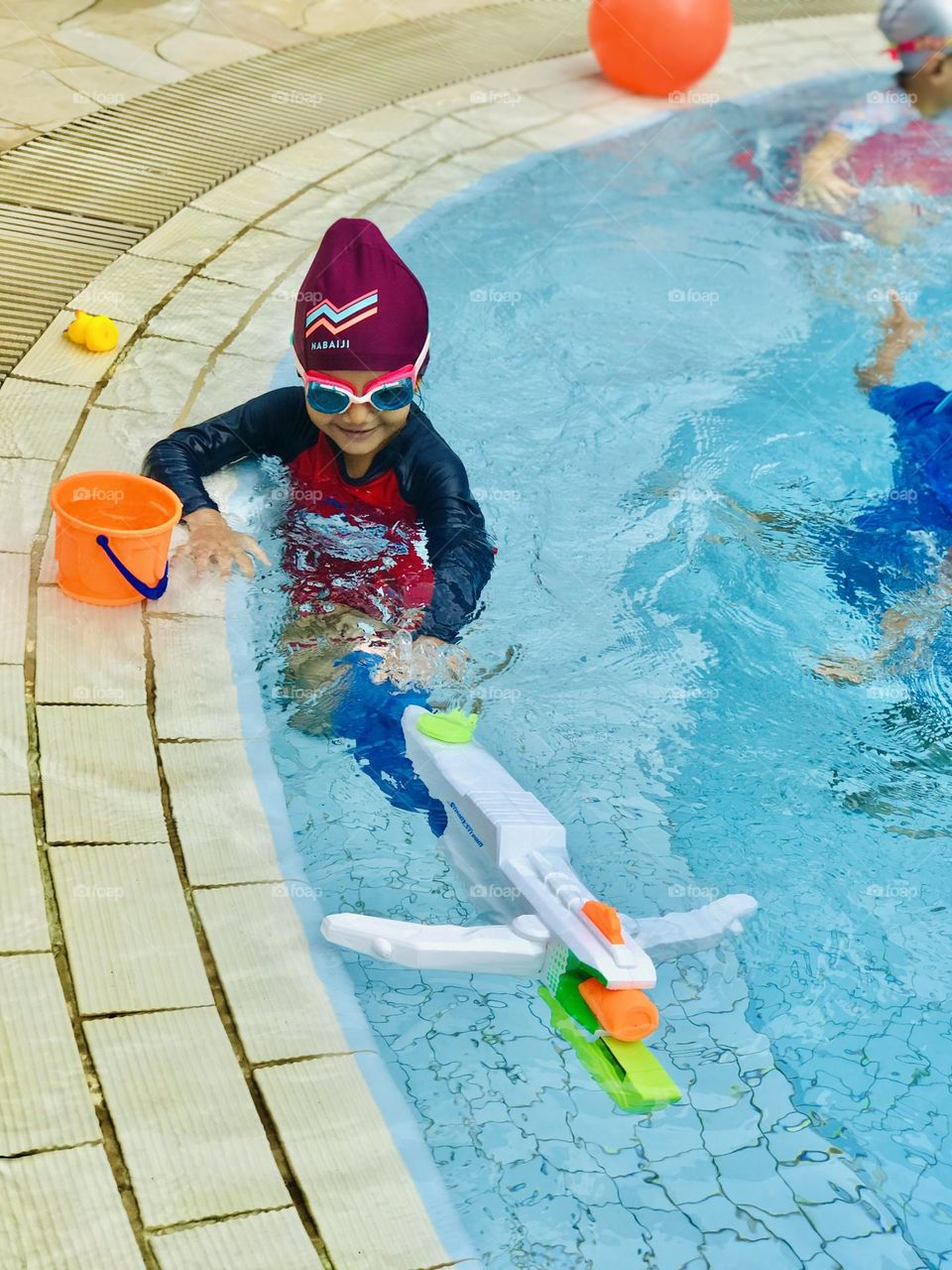 Baby girl enjoying at swimming pool with water sprinklers toy.