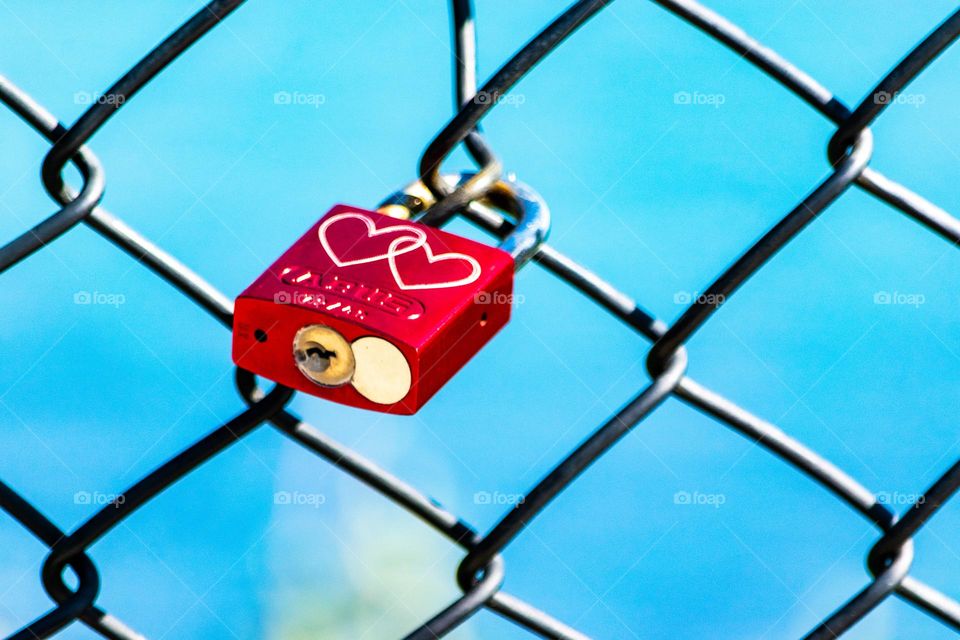 Red padlock with two white hearts lock around chain link fence