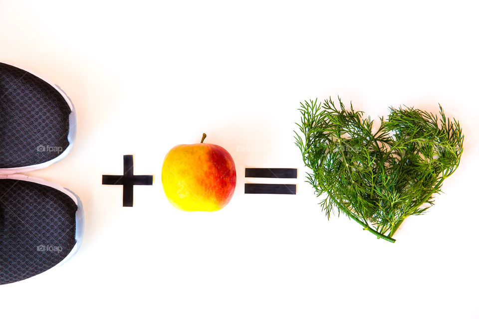 Staying in good shape is about exercise and healthy food. Simple minimalist image on white background lay flat with running shies and apple and leafy heart