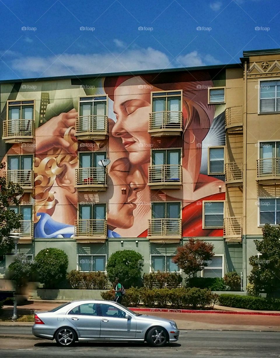 A car driving in front of an urban mural on an apartment building from A to B