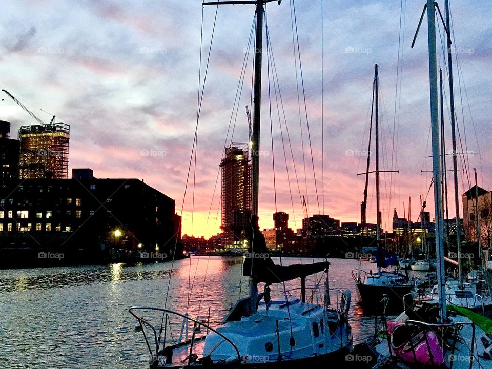 A colorful sunset at Newtown Creek in Long Island City, Queens, NY with its assembly of different boats. The firmament “above and below” reflects the setting sun’s light and colors everything in beautiful shades of magenta. 2021. Hypnotic Productions
