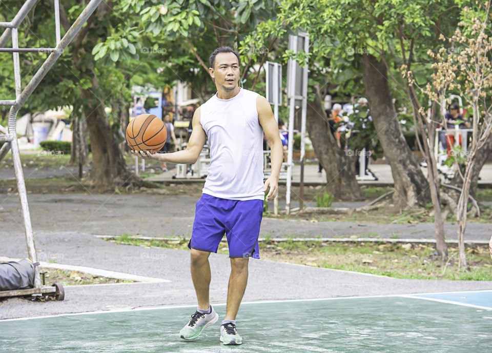 Basketball in hand Asian man to exercise Background  tree at Bang Yai Park , Nonthaburi in Thailand.