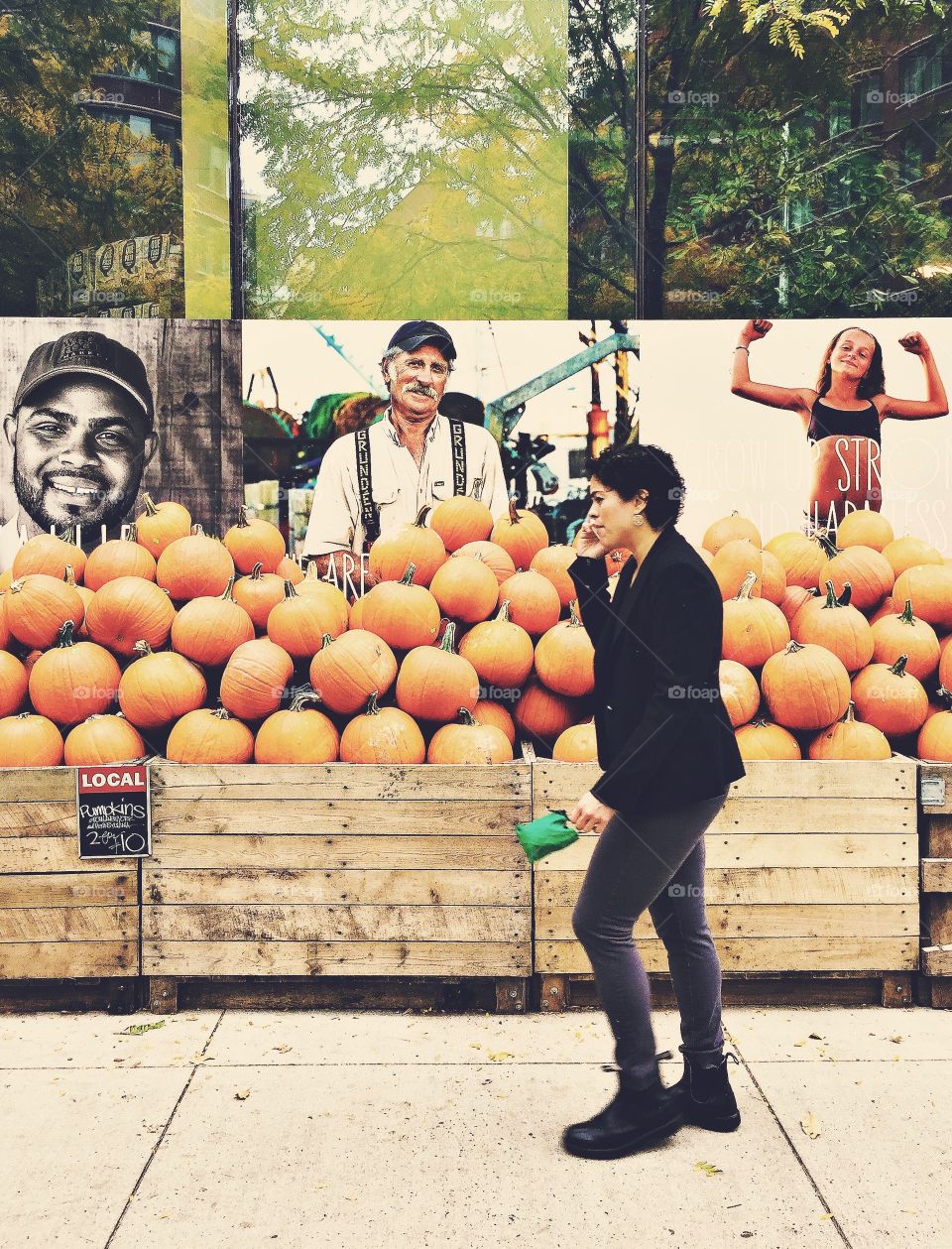 Woman walks talking on a cellphone in front a stand full of pumpkins
