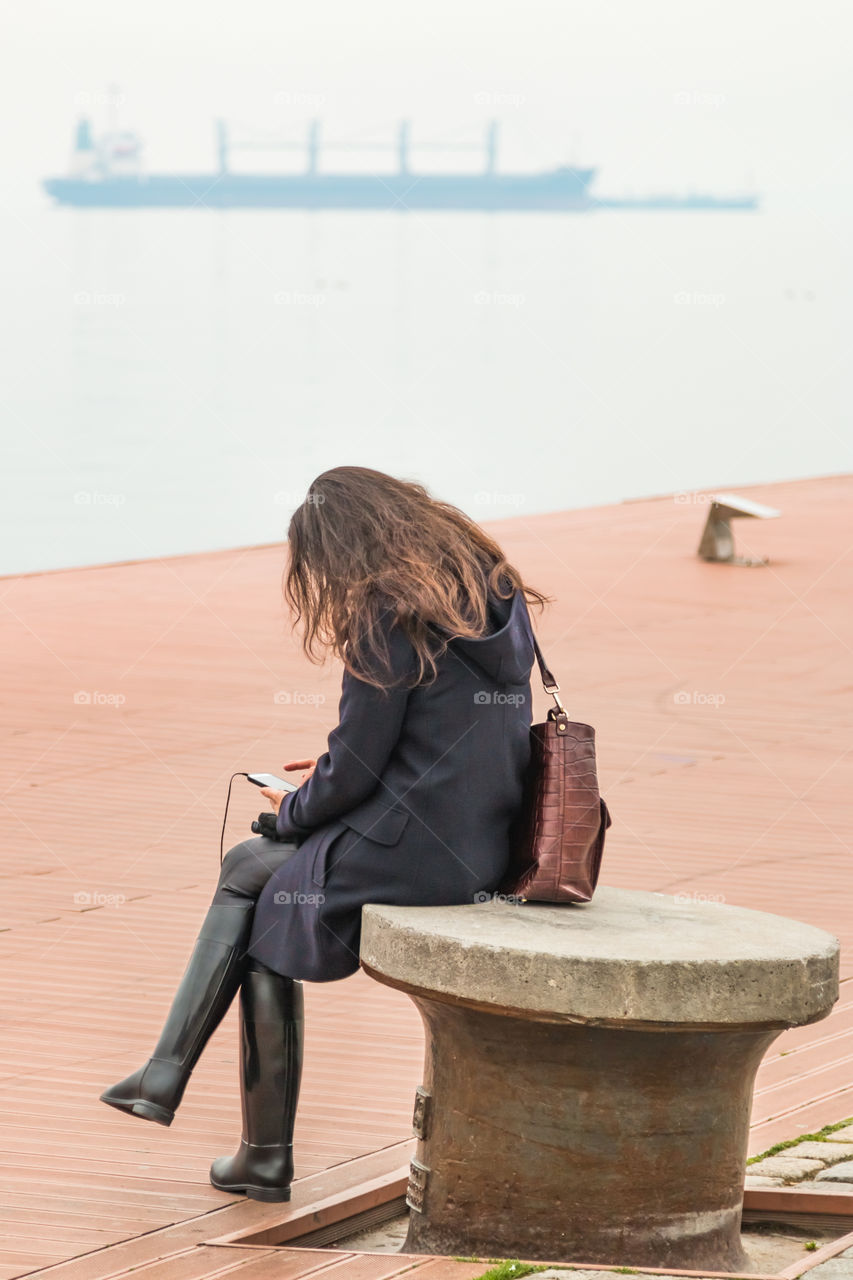 Young woman sitting alone at the dock using her Smartphone