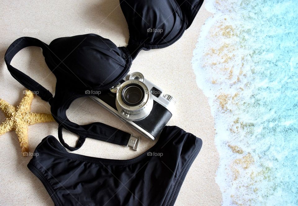 Black two piece swimsuit and a camera on the beach as the tide rolls in