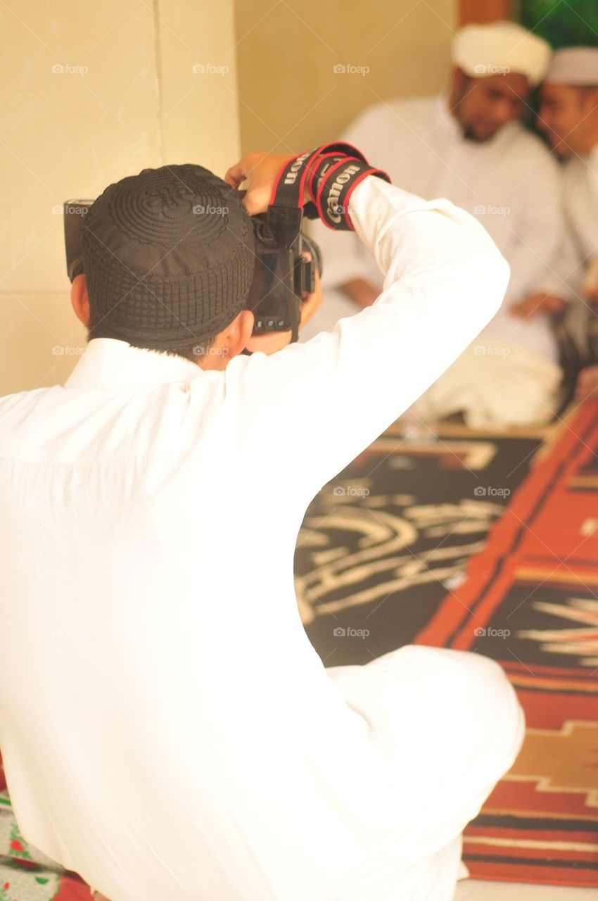 Portrait of an Asian man dressed in Muslim clothes aiming at a photo or video.