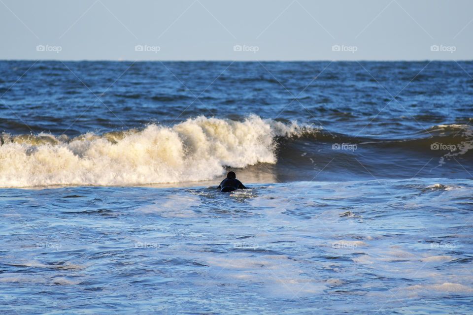 A surf enthusiast's makes his way out to the Atlantic to get some practice in catching waves in the dusk of day at Virginia Beach.