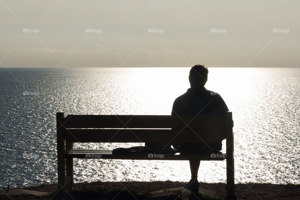 Man sitting on a bench by the ocean and watching the sunset 