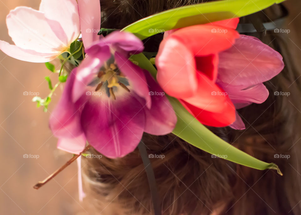 Woman wearing flower crown in long hair with pink and lavender tulips and leaves view from behind 