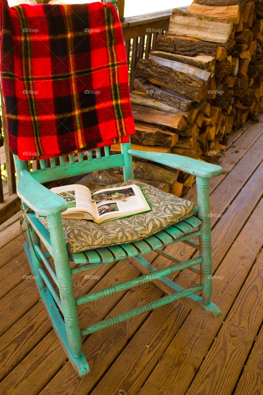 Rocking chair with book and cozy blanket on a farm porch.