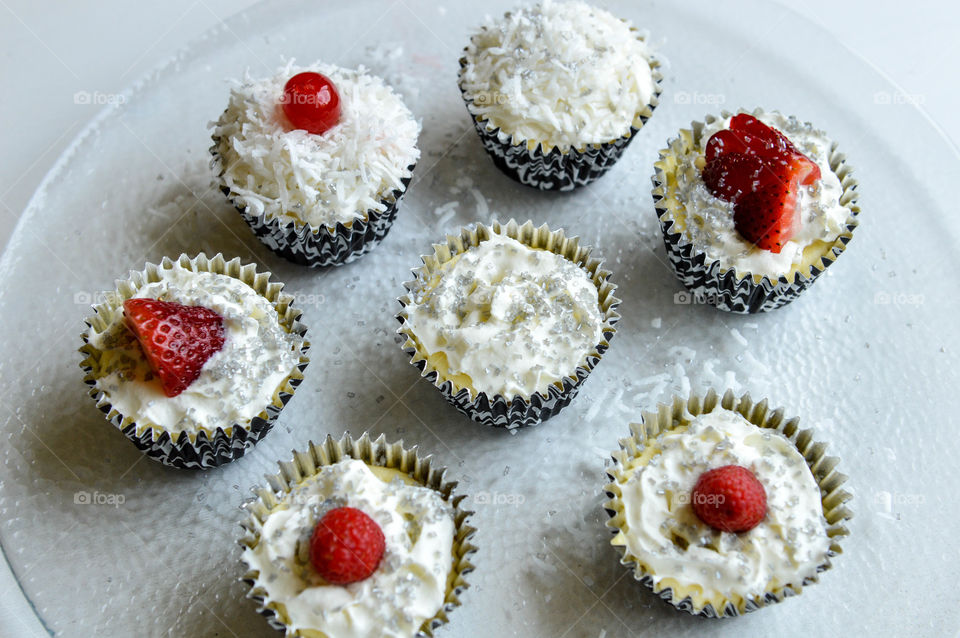 Mini cheesecakes in black and white decorative wrappers topped with whipped cream, coconut shavings and berries