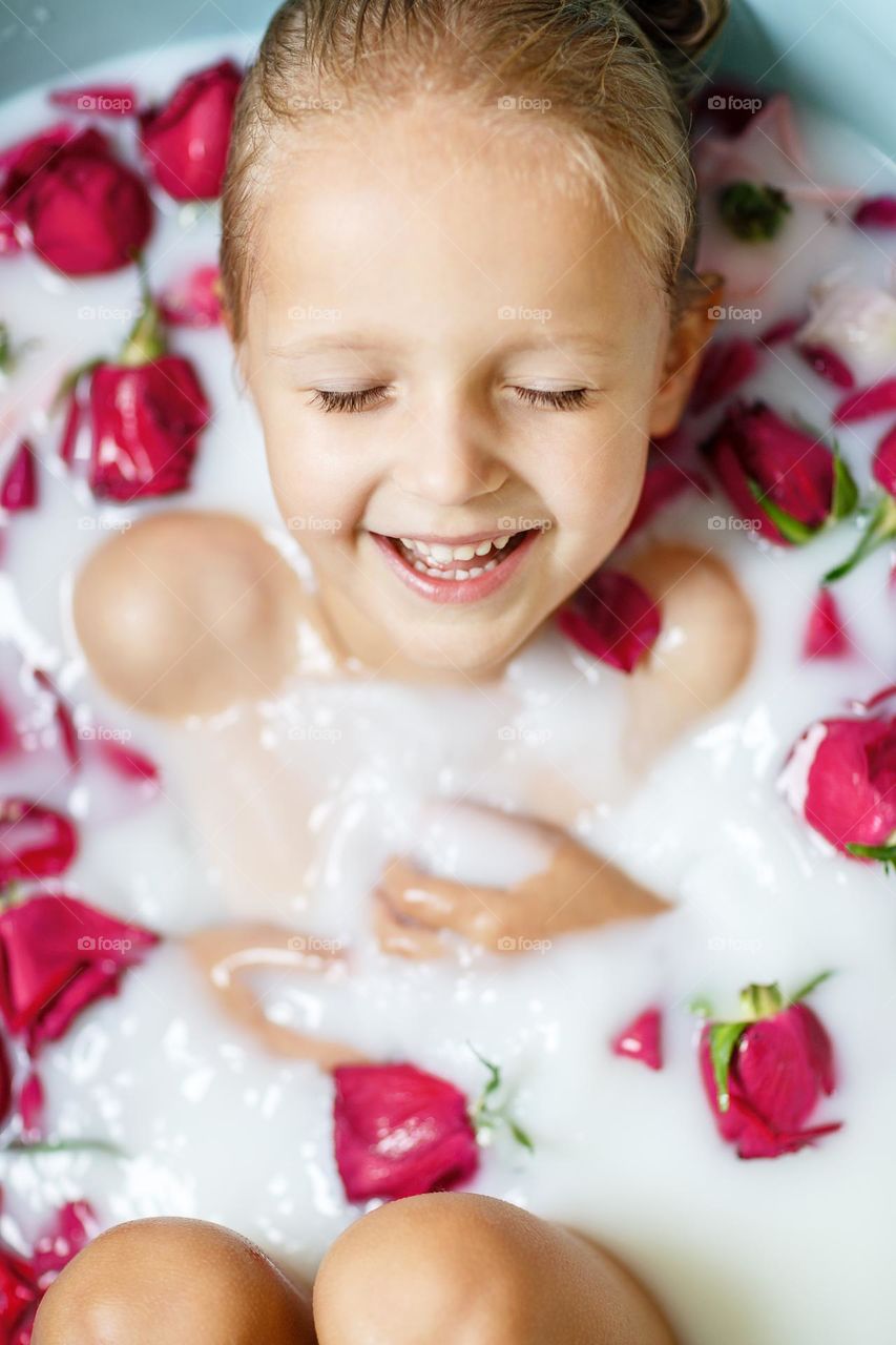 Candid lifestyle portrait of happy Caucasian girl taking a bath with milk and red roses at home