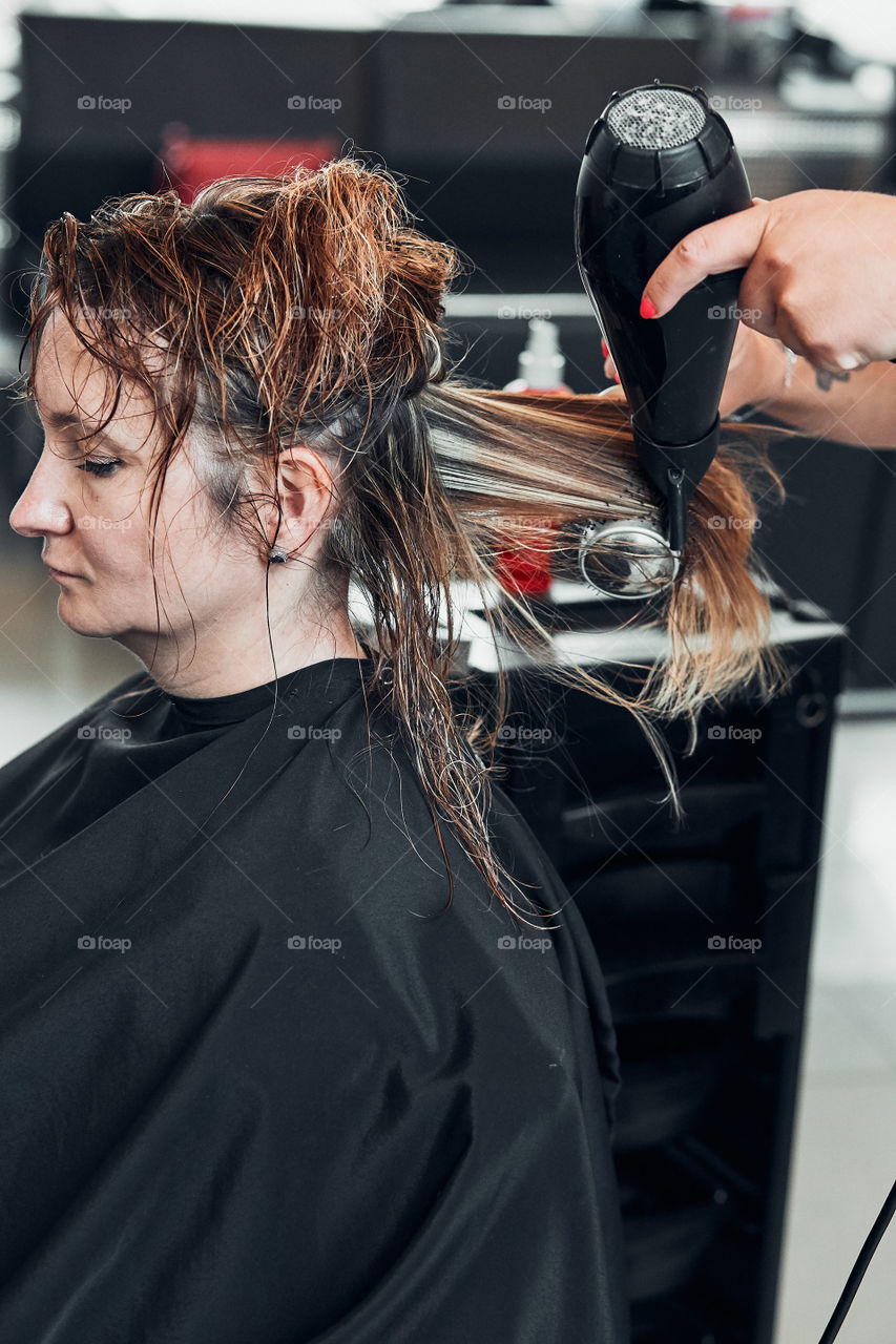 Hairdresser styling dyeing combing womans hair. Young woman working as a hairdresser in hair salon. Real people, authentic situations