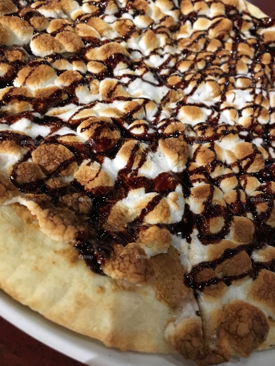 Pizza covered with peanut butter and topped with chocolate drizzle, graham cracker crumbles and marshmallows 