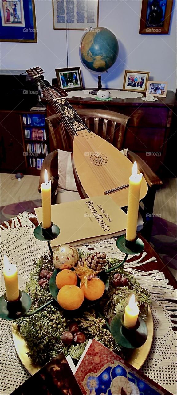 This is a festive display of lit candles and ornaments on an antique table as well as a traditional lute on a chair in „Bavaria“, Germany during Christmas time. 2022. Hypnotic Productions