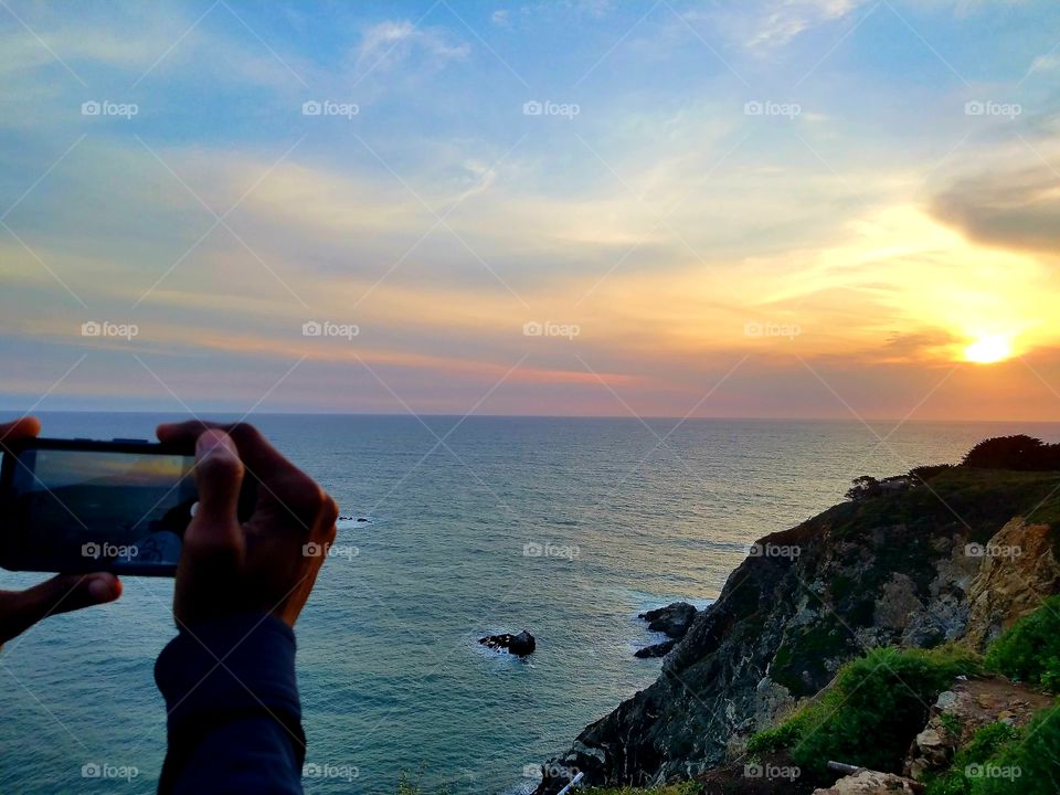 Man taking photo of ocean during a colorful sunset