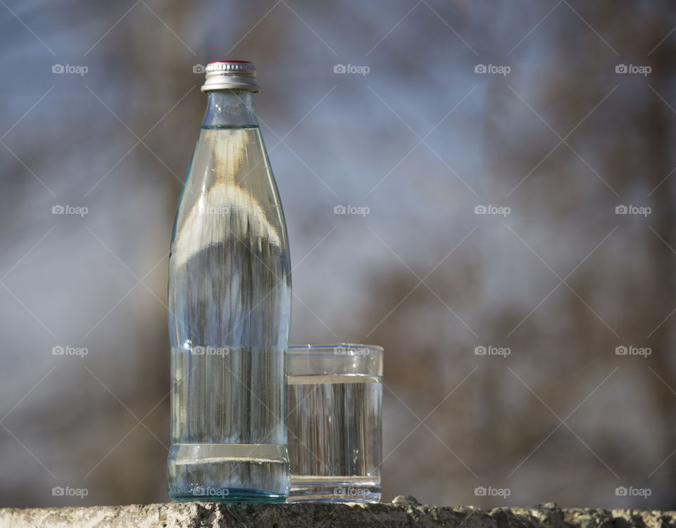 bottle and glass with cold fresh water against the sky