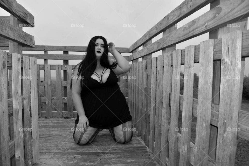 Gothic chick posing on an overlook tower. Wood rails around her. Black and white photo.